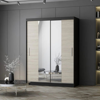 The CHOICEWARDROBE Vetra 2 Door Sliding Mirror Wardrobe, 150cm wide in Sonoma Oak with black trim, features shelves and a hanging rail. It’s placed against a gray wall in a modern room with a round table and decorative branches nearby.