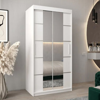 The CHOICEWARDROBE Vevey 100cm White Mirrored Sliding Door Wardrobe, featuring a modern panel design and full-length mirror, is showcased in a contemporary room with a striped wall, pampas grass vase, and a round mirror above the vanity.