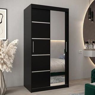 The CHOICEWARDROBE Vevey 2 Door 100cm Sliding Mirrored Wardrobe in black matte finish features a mirrored door and stripe panel, offering compact, modern storage for bedrooms with light wood floors and vertical wall paneling.