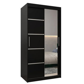 The CHOICEWARDROBE Vevey 2 Door 100cm Sliding Mirrored Wardrobe in black matte boasts a compact, modern design with a stripe panel and hanging storage. A stylish bed, headboard, and rug complete the contemporary bedroom setting.