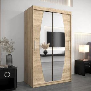 An Eden Mirrored Wardrobe 2 Sliding Doors 120cm in Sonoma Oak is placed in a modern bedroom with a black nightstand, decorative vase with dried flowers, wall-mounted TV, and a lit table lamp.