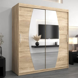 The Eden Mirrored Wardrobe 2 Sliding Doors 180cm in Sonoma Oak stands in a modern room, reflecting a wall-mounted TV, a floating shelf with a vase, and part of a bedside table with a lamp.