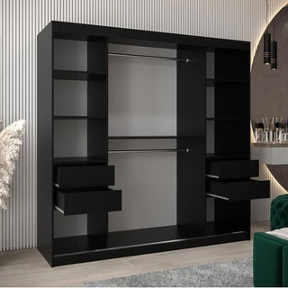 The Eden Mirrored Wardrobe with 2 sliding doors (200cm, black), featuring two hanging rods, shelves, and four open drawers, stands by a ribbed light wall beside a green chair and vanity table with cosmetics.