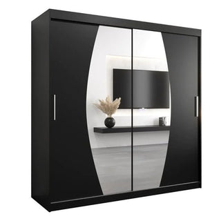 The Eden Mirrored Wardrobe 2 Sliding Doors 200cm In Black features vertical oval mirrors that reflect a wall-mounted TV, floating shelf, and vase with dried plants in a modern bedroom.