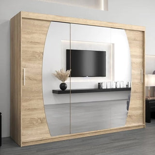 The Eden Mirrored Wardrobe 3 Sliding Doors 250cm in Sonoma Oak stands in a modern room, its mirrors reflecting a wall-mounted TV, a floating black shelf, a vase with dried grass, and glass objects.