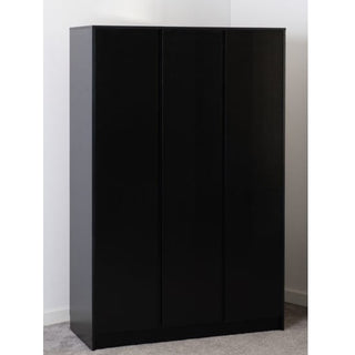 The Mcgowen Wooden Wardrobe With 3 Doors In Black, featuring a simple, modern design with no visible handles, stands against the corner of a white wall on a light grey carpeted floor.