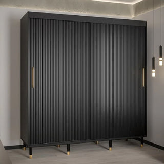 The Millwall 200cm Wooden Wardrobe with 2 Sliding Doors in Black features vertical grooves, gold handles, and gold leg accents. It stands on a light floor in a modern room with pendant lights and an exposed concrete ceiling—ideal for bedroom storage.