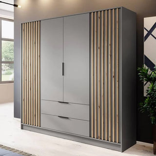 The Newberry Wooden Wardrobe With 4 Hinged Doors 206cm in Grey, featuring matte gray doors, two bottom drawers, and vertical wooden slat accents, stands in a bright room with nearby plant and wall decor.