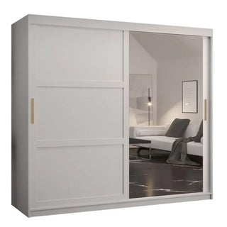 The Rieti II Mirrored Wardrobe (200cm, white) has two sliding doors—one mirrored, one solid—with gold handles. Its mirror reflects the minimalist room, enhancing the clean look of this modern wardrobe.