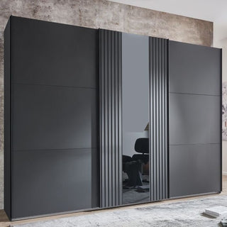 The ATLANTIC 3 Door Sliding Wardrobe (Black, 300cm) features flat panels, vertical textured lines, metal handles, and a tall mirror. It is shown against a textured brown-gray wall in a contemporary room.