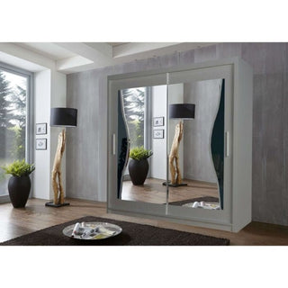 A modern bedroom features the HEFFNER 2 Door Mirrored 180cm Grey Sliding Wardrobe, two potted plants, a floor lamp, framed wall art, and a brown rug with a tray on the wooden floor for stylish storage.