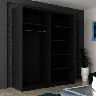The INFINITE 2 Door Mirrored Wardrobe in black (150cm) offers stylish bedroom storage with multiple shelves and a hanging rod, set against a dark patterned wall. A white potted plant, glass table, and green chair are also visible.