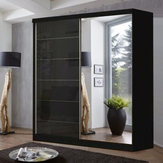 The INFINITE 2 Door Mirrored Wardrobe in black high gloss (150cm) stands in a modern living room, its mirrored sliding doors reflecting a large window, floor lamp, wooden sculpture, and potted plant—perfect for stylish bedroom storage.
