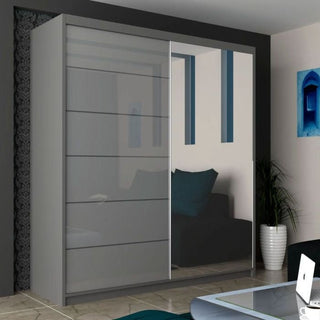 The INFINITE 2 Door Mirrored Wardrobe in grey (150cm) with high gloss sliding doors stands on tiled floors, reflecting a black sofa with a blue pillow, a potted plant, and some of the room’s wall decor.