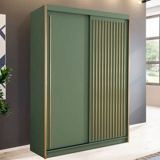 The KESTEVEN 2 Door Sliding Wardrobe in green (150cm) with gold accents stands against a gray wall in a bright room, featuring a plant on the left and a window on the right—bringing style and elegance to any space.