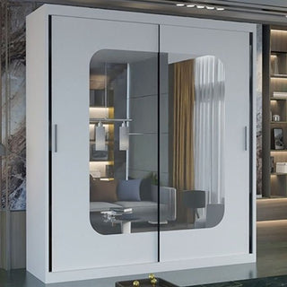 The MERICA 2 Door Mirrored Wardrobe in white (180cm) offers modern bedroom storage, with large mirrored sliding doors reflecting a stylish living room featuring a couch, curtains, and shelves.