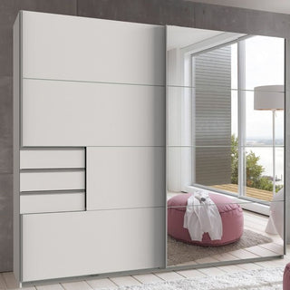 The SOGO 2 Door Mirrored Wardrobe White 225cm reflects a bright room and pink ottoman, while offering ample bedroom storage with multiple drawers and compartments behind its modern mirrored sliding doors.