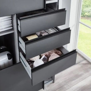 The SOGO 2 Door Sliding Wardrobe in graphite with black, 225cm, features three dark grey drawers partly open to display neatly folded clothes and accessories. Positioned by a large window with a grassy view, it offers sleek bedroom storage.