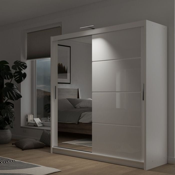 The HIGHLAND 2 Door Mirrored Sliding Wardrobe in white (203cm) stands in a modern bedroom with wooden flooring, a bed, window-side plant, wall light above the wardrobe, and modular storage.