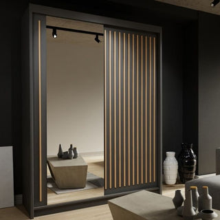 The ZEUS 2 Door Mirrored Wardrobe in black (150cm) features one mirrored and one slatted sliding door, standing stylishly in a room with vases and a low coffee table.