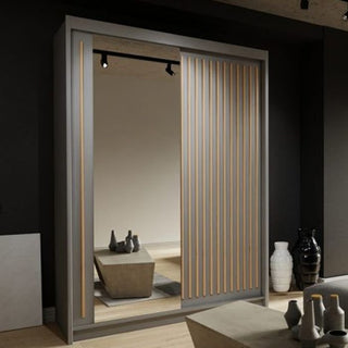 The ZEUS 2 Door Mirrored Wardrobe Grey 150cm with vertical wood accents stands against a dark wall. Its full-length mirror reflects ceramic vases and a rectangular table.