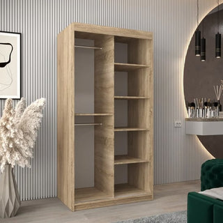 The Tavira I Mirrored Wardrobe with 2 sliding doors in Sonoma Oak (100cm) features shelves and two hanging rods, complementing a modern room with vertical wall panels, a round mirror, and stylish décor.