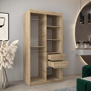 The Tavira I Mirrored Wardrobe with 2 sliding doors in Sonoma Oak (100cm) features open shelving, two hanging rods, and two partially open drawers, standing in a modern room with striped walls and a vanity table.