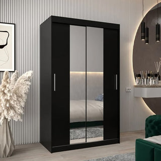 A modern bedroom featuring the Tavira I Mirrored Wardrobe 2 Sliding Doors 120cm in Black, placed beside a vase of pampas grass, with a round wall mirror and a wall-mounted vanity holding makeup items.