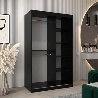 The Tavira I Mirrored Wardrobe with 2 sliding doors (120cm, black) stands in a modern room with wall art, a decorative vase, and a vanity with lights. It offers hanging space on the left and five right-hand shelves for organized storage.