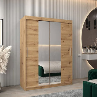 The Tavira I Mirrored Wardrobe with 2 sliding doors in Artisan Oak stands in a modern bedroom with light wood floors, a green velvet bed, vanity table, round wall mirror, vertical wall panels, and decorative accents.