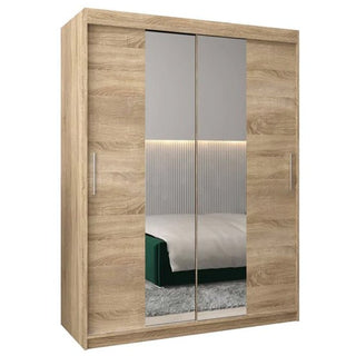 The Tavira I Mirrored Wardrobe with two sliding doors in Sonoma Oak features metal handles and enhances a modern bedroom setting with reflections of a bed, rug, and wall decor.