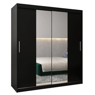 The Tavira I Mirrored Wardrobe 2 Sliding Doors 180cm In Black features two mirrored panels that reflect a bed, an illuminated headboard, and part of a rug. Sleek silver handles enhance its modern look.
