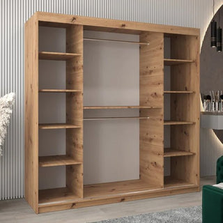 The Tavira I Mirrored Wardrobe with 2 sliding doors (200cm) in artisan oak, featuring multiple shelves and hanging space, is placed against a wall in a modern room.