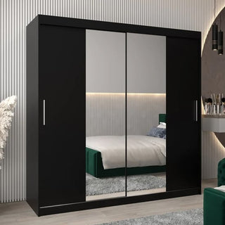 The Tavira I Mirrored Wardrobe with 2 sliding doors (200cm, black) stands in a modern bedroom with striped walls, a green bed, a shaggy gray rug, and a vanity table displaying various items.