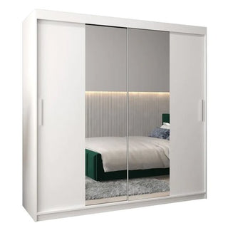 The Tavira I Mirrored Wardrobe with 2 sliding doors in white (200cm) features full-length mirrors, reflecting a modern bedroom with a bed, textured headboard, and gray rug.