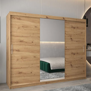 The Tavira I Mirrored Wardrobe 3 Sliding Doors 250cm in Artisan Oak sits in a modern bedroom with a green bed, light gray rug, and vertical panel wall detailing.