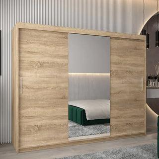 The Tavira I Mirrored Wardrobe with 3 sliding doors, 250cm wide in Sonoma Oak, features a large rectangular mirror and light wood finish, shown in a modern bedroom with a bed and rug reflected.