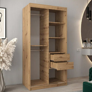 The Tavira II Mirrored Wardrobe with 2 sliding doors in Artisan Oak (100cm) features shelves, two hanging rods, and drawers, showcased in a modern room with chic decorative accents in the background.