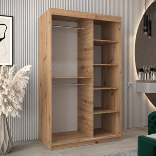 The Tavira II Mirrored Wardrobe 2 Sliding Doors 120cm in Artisan Oak features left-side hanging rods and right-side shelves, set in a modern room with striped walls, plants, artwork, and a vanity area.