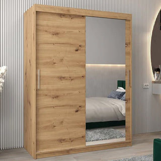 The Tavira II Mirrored Wardrobe, 150cm wide in artisan oak with silver handles, features two sliding doors—one with a large mirror—and is shown in a modern bedroom setting with a bed, nightstand, and round wall mirror.