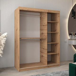 The Tavira II Mirrored Wardrobe with 2 sliding doors (150cm, Artisan Oak) stands against a vertically grooved wall, with a decorative plant and part of a vanity with mirror visible nearby.