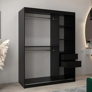 The Tavira II Mirrored Wardrobe in black, with 2 sliding doors, 2 hanging rods, multiple shelves, and 2 open drawers on the right side, is placed in a room with light striped walls and wooden flooring.