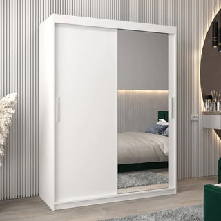 The Tavira II Mirrored Wardrobe 2 Sliding Doors 150cm in White stands in a modern bedroom, complemented by a bed with a green headboard and a dressing table in the background.