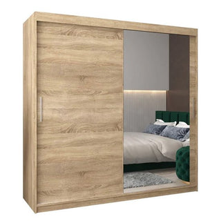 The Tavira II Mirrored Wardrobe 2 Sliding Doors 200cm in Sonoma Oak, with one mirrored and one wood-finish door, elevates this modern bedroom styled with a green upholstered bed and a gray rug.