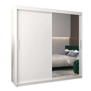 The Tavira II Mirrored Wardrobe (200cm, 2 sliding doors, white) features one solid panel and one full-length mirror, perfect for reflecting a modern bedroom with a bed, headboard, and part of a rug.