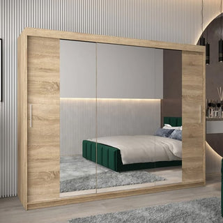 The Tavira II Mirrored Wardrobe with 3 sliding doors (250cm, Sonoma Oak) stands in a modern bedroom, its mirrored panels reflecting a green upholstered bed, gray rug, and softly lit vertical wall paneling.
