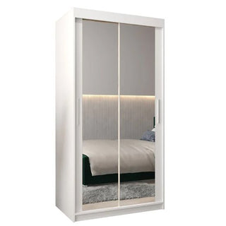 The Tavira III Mirrored Wardrobe 2 Sliding Doors 100cm in White features mirrored doors that reflect a cozy bedroom with a bed, headboard, gray carpet, and LED strip lighting on the wall.