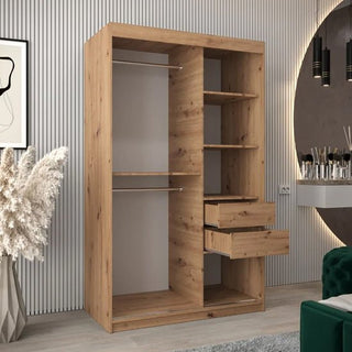 A Tavira III Mirrored Wardrobe with 2 sliding doors in Artisan Oak stands in a modern room with shelves, drawers, and hanging rods. Decorative items, framed art, and vertical wall paneling complete the backdrop.