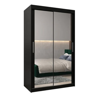 The Tavira III Mirrored Wardrobe with 2 sliding doors in black reflects a modern bedroom with a green bed, beige bedding, gray rug, and horizontal accent lighting on the wall.