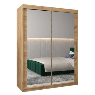 The Tavira III Mirrored Wardrobe 2 Sliding Doors 150cm in Artisan Oak reflects a modern bedroom with a green bed, gray bedding, textured wall panels, and ambient lighting.